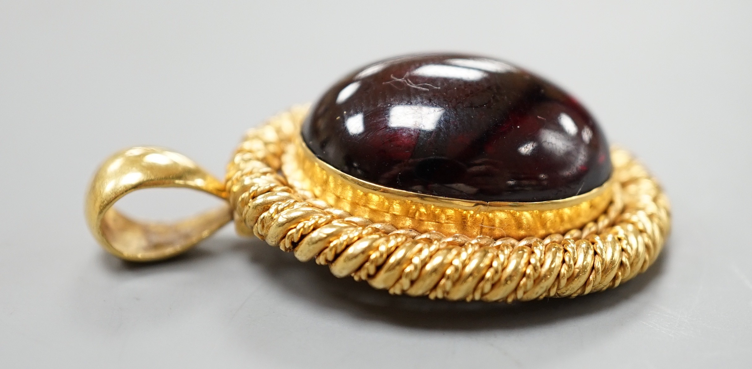 A yellow metal and oval foil backed? cabochon garnet set pendant, with close back setting, overall 42mm, gross weight 17.4 grams.